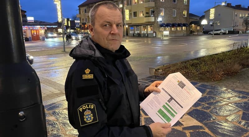 Polis står under gatlykta och håller upp papper med grönfärgad tabell.