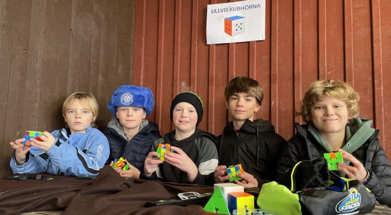 Fem elever i mellanstadieåldern sitter utomhus vid en bänk på skolgården under skylten "Ullvis kubhörna"