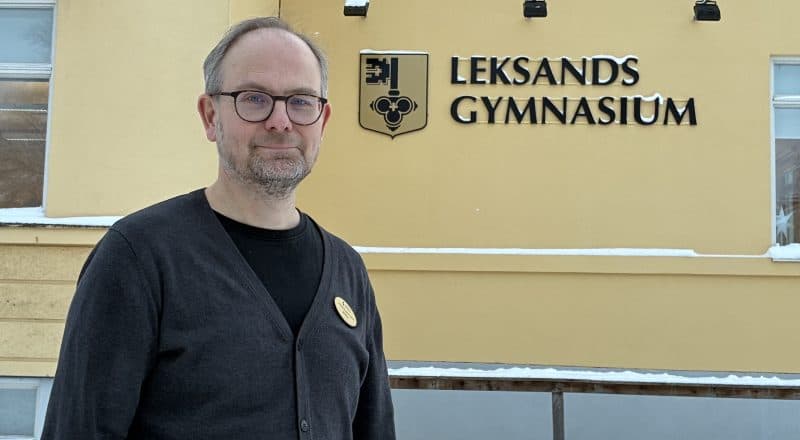 Man står framför skolfasad med texten "Leksands Gymnasium" på väggen.