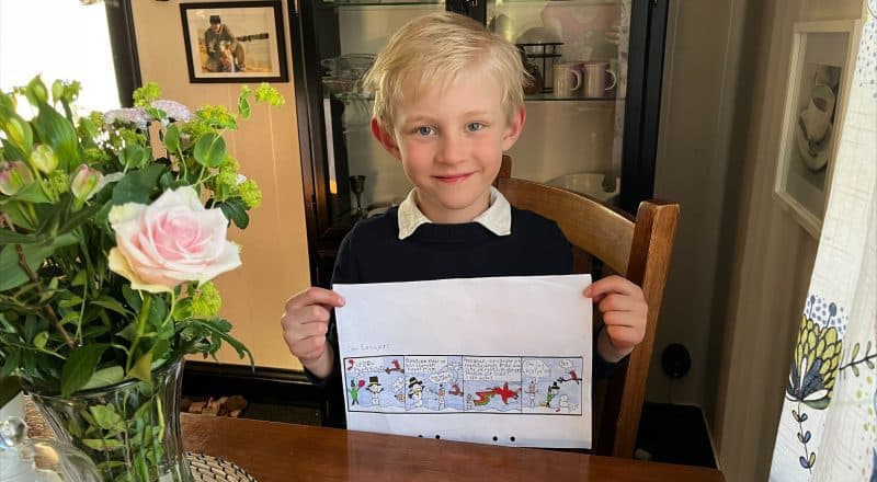 7-årig pojke i fina kläder håller upp ett papper med sin serieteckning.