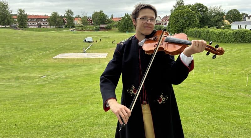 Julius Berglund står framför Gropen med stråken mot fiolen. Han har en klassisk Leksandsdräkt på sig.