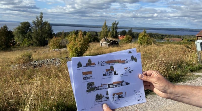 Händer håller upp papper med skisser framför en vacker utsikt mot Siljan från Tällbergs sluttning.