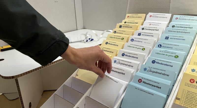 Valsedlar i ett ställ, en hand plockar en blank röst.