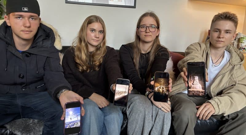 Fyra elever sitter i en soffa och håller fram sina mobiltelefoner där de visar bilder från resan.