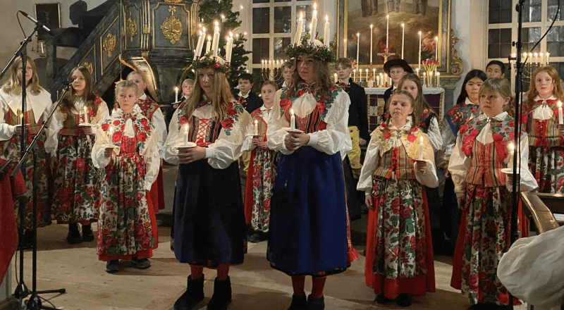 Två lucior i rödvita överdelar och mörkblå kjolar, framför ett 20-tal andra mellanstadieelever.