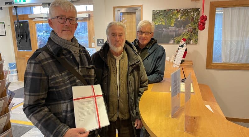 Tre män står vid kommunens reception i Leksand med en namninsamling med röda band runt.