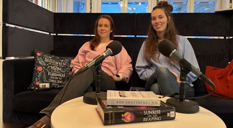 Två kvinnor i en soffa, på bordet framför dem ligger två mikrofoner och ett par böcker i en trave.