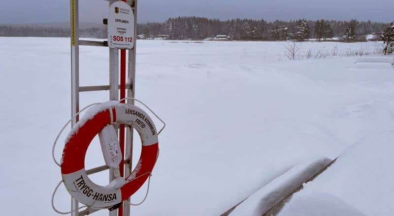 En livboj som hänger på en stolpe med texten "Opplimen". Sjön i bakgrunden.