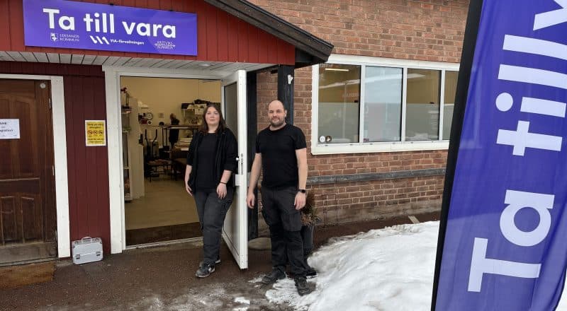 Två personer står uppställda framför en öppen dörr till butiken.