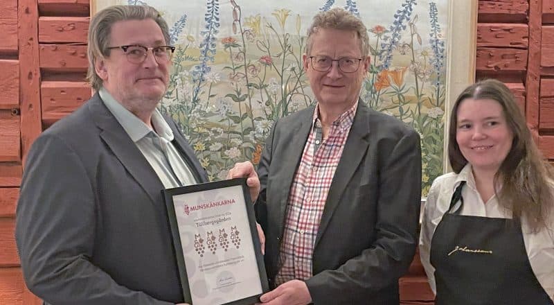 Diplom hålls upp framför tre finklädda personer.