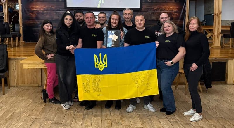 En grupp med tio krigsveteraner håller upp en ukrainsk flagga framför Linnéa Åslin.