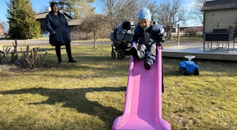 Barn glider ned för en rosa rutschkana, mamma står i bakgrunden och skrattar.