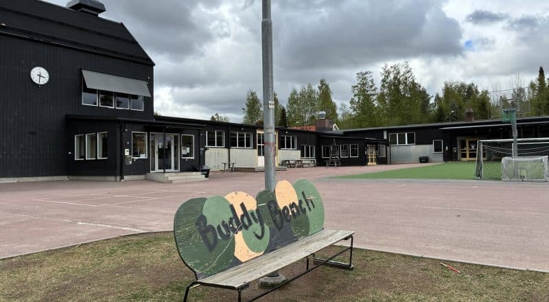 Bild på tom skolgård med en bänk i förgrunden.