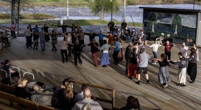 Dansbana med tre ringar med ett tiotal personer i varje ring. En liten orkester spelar och några sitter och tittar på.