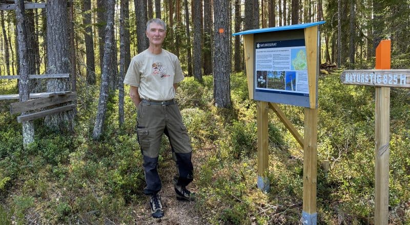 Man i friluftskläder står på en stig mellan en informationsskylt och ett älgpass.