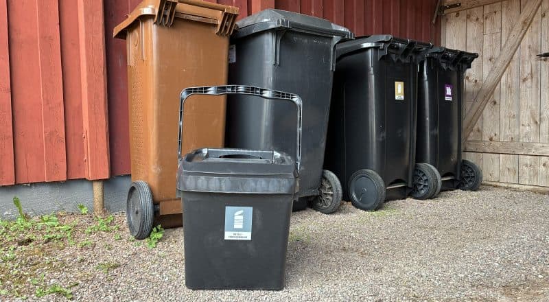 Metallåtervinningsboxen står framför fyra andra soptunnor.