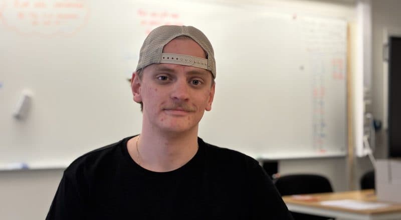 Porträtt på Ludde Blomberg i en klassrumsmiljö med en whiteboardtavla i bakgrunden.
