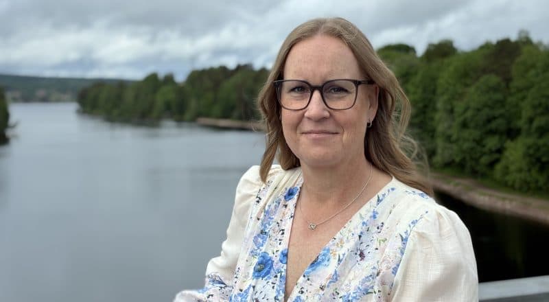 Karin Mikkonen står i somriga kläder på Leksandsbron med utsikt över älven.