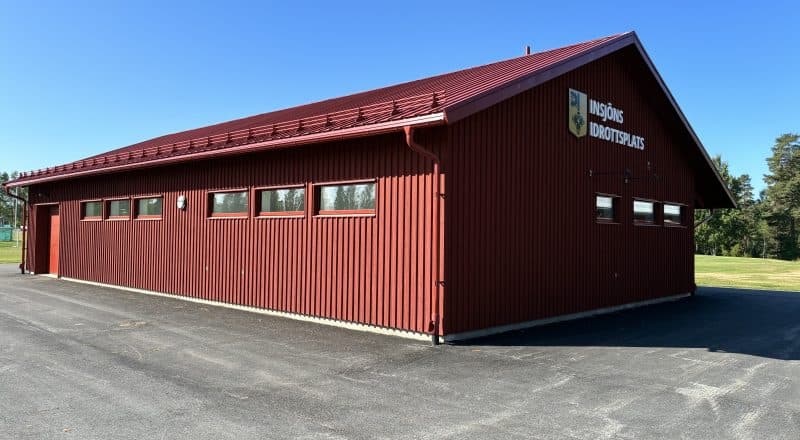 Exteriörbild på röd byggnad med skylten Insjöns Idrottsplats och Leksands kommuns logotyp.