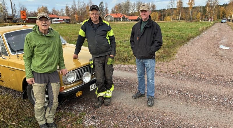 Tre personer som står lutade mot en bilhuv i korsningen mellan flera grusvägar.