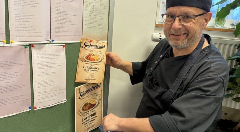 Man i kockkläder håller upp affischer vid en utställningshörna