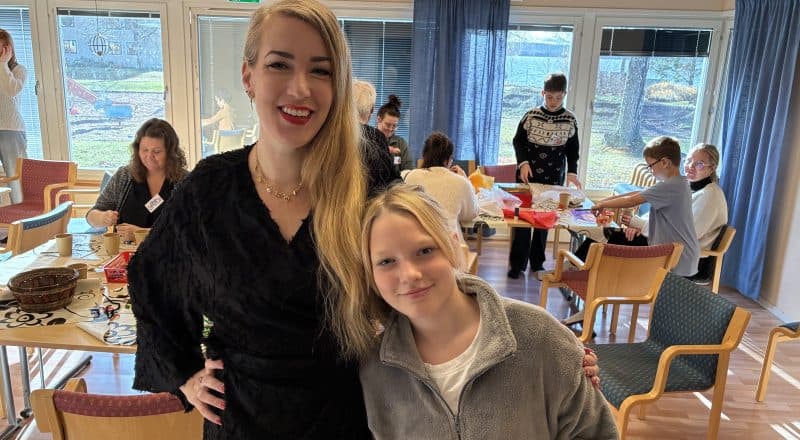 En glad kvinna och hennes dotter i mellanstadieåldern står i ett pysselrum och ler brett mot kameran.